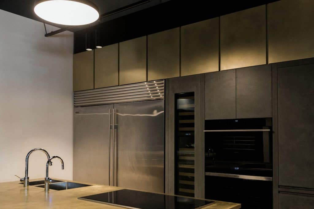 Modern kitchen with stainless steel appliances, built-in oven, wine cooler, large fridge, under-cabinet lighting, sleek dark cabinetry, a sink with a double tap, and an electric hob on a smooth worktop.